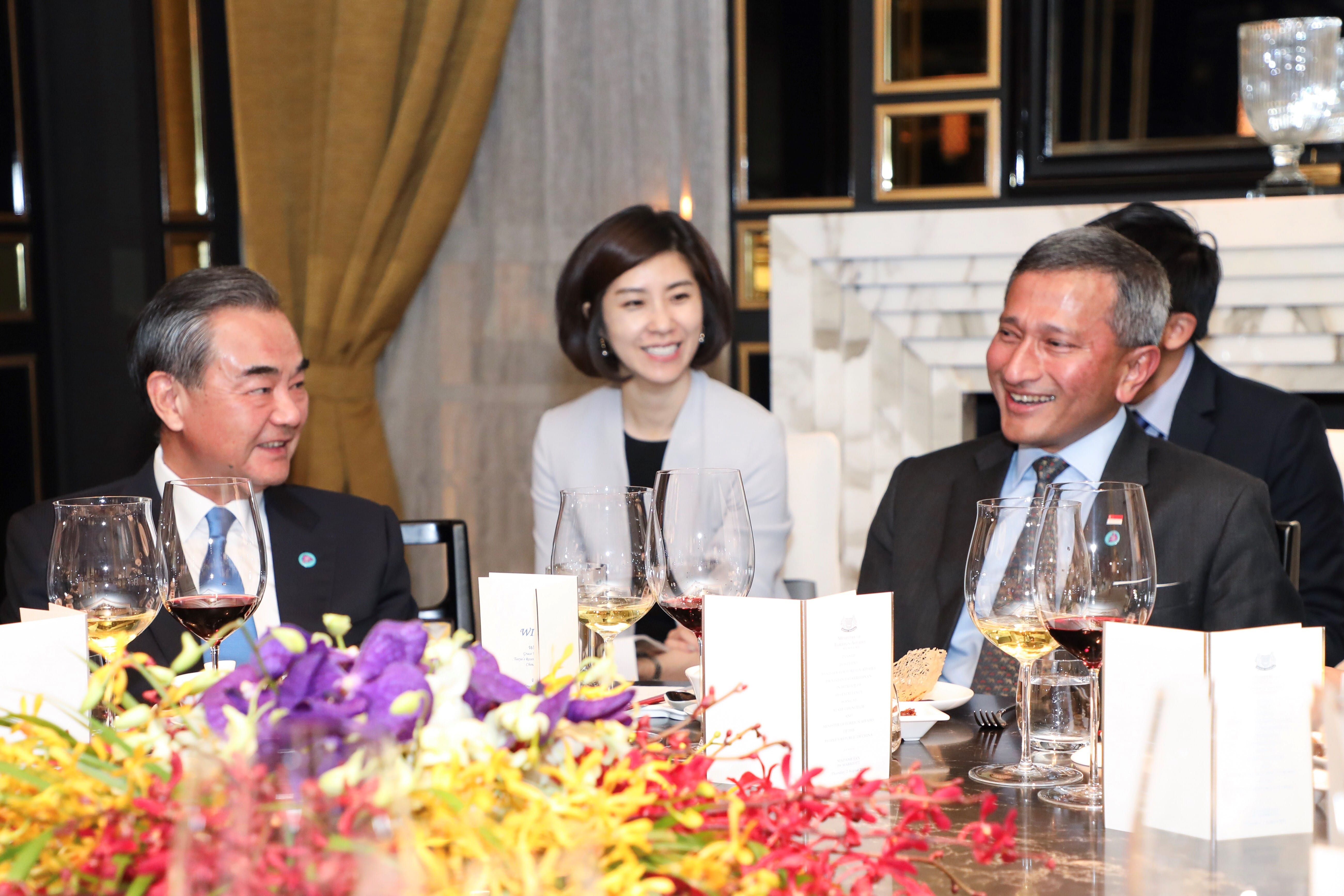 Three people sit at a table with wine glasses and floral arrangements.
